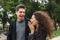 Image of satisfied couple man and woman 20s in warm clothes, walking through green park