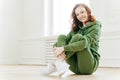 Image of satisfied refreshed young woman with foxy hair, keeps legs crossed, wears tracksuit and sportshoes, glad to have workout