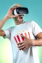 Image of screaming bearded hipster man wearing virtual reality goggles eating popcorn from bucket in neon lights.