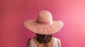 Back of woman wearing wide brimmed sunhat on pink background