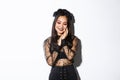 Image of sensual, beautiful asian woman in gothic lace dress and black wreath smiling coquettish, touching face and