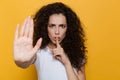 Image of serious woman 20s with curly hair holding finger at lip Royalty Free Stock Photo