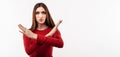 Image of serious woman in casual red sweater making X sign with crossed hands. Studio shot, white background. Copy space Royalty Free Stock Photo