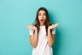 Image of shocked and anxious brunette woman in white t-shirt, spread hands sideways and gasping alarmed, standing over