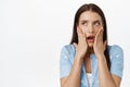 Image of shocked brunette woman gasp, open mouth startled, holding hands on face, staring at upper left corner sale or