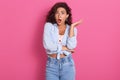 Image of shocked young female with stunned expression, keeps mouth opened, wearing stylish blue shirt and jeans, spreading palm Royalty Free Stock Photo