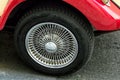 The image shows a close-up of a cars wheel with a shiny, intricate wire-spoke hubcap. The car has a red body and is parked on