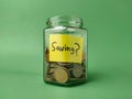 The image shows a glass jar filled with coins, with a yellow sticky note on it that says Saving Royalty Free Stock Photo