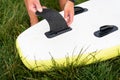 The image shows a man attacking a black fin to the bottom of a white and yellow surfboard placed on lush green grass