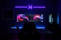 The image shows a person at a desk with two monitors, mouse, keyboard, CPU, wall frame, and neon sign Royalty Free Stock Photo