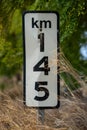 Traffic sign for kilometer 145 with blurred trees in the background and dry grass in the foreground. Royalty Free Stock Photo