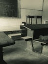 The image shows a room with benches and a chalkboard. The image is in black and white