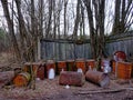 This image shows rusty barrels that are scattered in front of a wooden fence