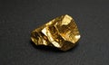 single, irregularly shaped gold nugget rests on dark surface, its surface reflecting light. Royalty Free Stock Photo