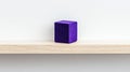 A purple cube sits on a light wood shelf against a white wall. Royalty Free Stock Photo