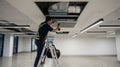 Professional technician working on ceiling air ventilation system in modern office space ensuring proper maintenance and Royalty Free Stock Photo