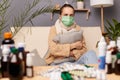 Image of sick unhealthy ill young adult woman wearing warm sweater, scarf and protective mask sitting on sofa in home interior