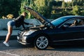 Image on side of young blonde standing in front of black car with open hood Royalty Free Stock Photo