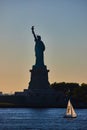 Silhouette of Statue of Liberty with small sailboat passing by in light and golden hour