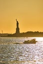 Silhouette of Statue of Liberty in soft golden light with ship sailing past in foreground over glistening waters