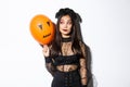 Image of silly beautiful asian woman in witch costume, holding orange balloon with scary face, celebrating halloween Royalty Free Stock Photo