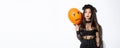 Image of silly beautiful asian woman in witch costume, holding orange balloon with scary face, celebrating halloween Royalty Free Stock Photo