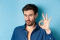 Image of silly young man pucker lips and show okay gesture, praise good thing, compliment excellent choice, standing on Royalty Free Stock Photo