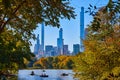 Skyscrapers surround Central Park New York City looking through trees at pond with boat Royalty Free Stock Photo