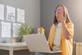 Image of sleepy exhausted woman with brown hair wearing yellow shirt posing in office, working on notebook, yawning, covering