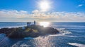 Small Maine island with lighthouse from above with sun shining over ocean