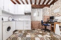 Image of a small open kitchen furnished with white appliances integrated into a rustic-style apartment with wooden beams on the Royalty Free Stock Photo