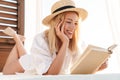 Image of smiling blonde woman reading book while lying on bed Royalty Free Stock Photo