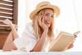 Image of smiling blonde woman reading book while lying on bed Royalty Free Stock Photo