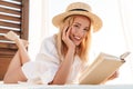 Image of smiling blonde woman reading book while lying on bed Royalty Free Stock Photo