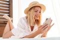 Image of smiling blonde woman using cellphone while lying on bed Royalty Free Stock Photo