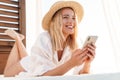 Image of smiling blonde woman using cellphone while lying on bed Royalty Free Stock Photo