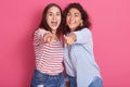 Image of smiling breunette girls posing isolated over pink sudio background, looking amd pointing at camera, female with wavy hair
