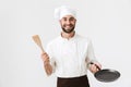 Image of smiling chief man in cook uniform holding wooden kitchen spatula and frying pan