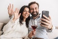 Image of smiling couple taking selfie photo together on sofa while drinking wine in bright room Royalty Free Stock Photo