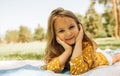 Image of smiling cute little girl lying and relaxing on the blanket at the green grass. Beautiful child taking rest outdoors Royalty Free Stock Photo