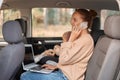 Image of smiling delighted Caucasian woman wearing beige sweater sitting on backseat with her baby and talking smart phone, Royalty Free Stock Photo