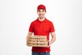 Image of smiling deliveryman in red t-shirt and cap holding stack of pizza boxes, isolated over white background