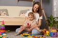 Image of smiling mother and child playing on the floor in the nursery with building a tower of colored blocks. Educational Royalty Free Stock Photo