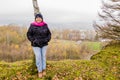 Image of a smiling woman with a black coat, denim jeans and a pink scarf resting on a trunk of a tree Royalty Free Stock Photo