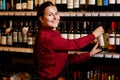 Image of smiling woman with bottle in her hands in wine shop