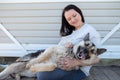 Image of smiling woman in jeans and white jacket sitting next to happy shepherd puppy against white wooden building