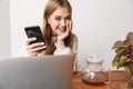 Image of smiling woman using laptop and smartphone while drinking tea Royalty Free Stock Photo