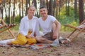 Image of smiling young family enjoying fresh air and beautiful nature in the forest, sitting on blanket on the ground, looking at Royalty Free Stock Photo