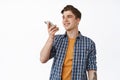 Image of smiling young man talking on speakerphone, record voice message or translate speach with mobile phone app