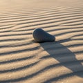 In the image, a smooth, gray, pebble-shaped stone rests on rippled sand Royalty Free Stock Photo